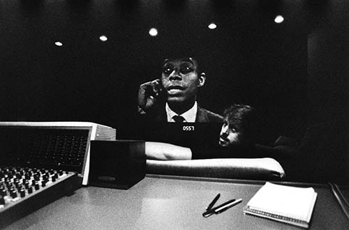 Douglas Dempsey sitting in front of mixing console; Baldwin on-screen in the background